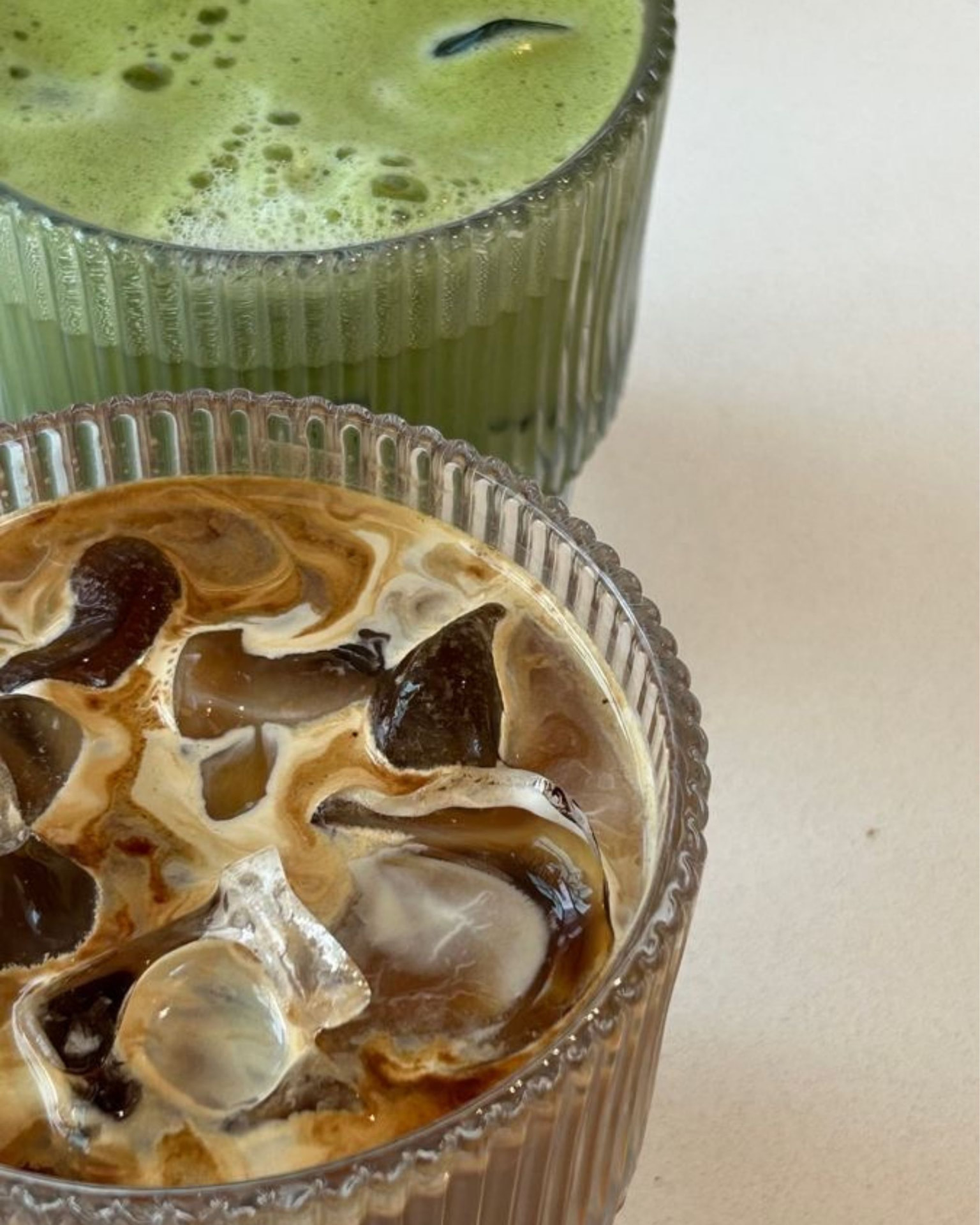 Eiskaffee mit Milch und Matcha Latte in gerillten Gläsern