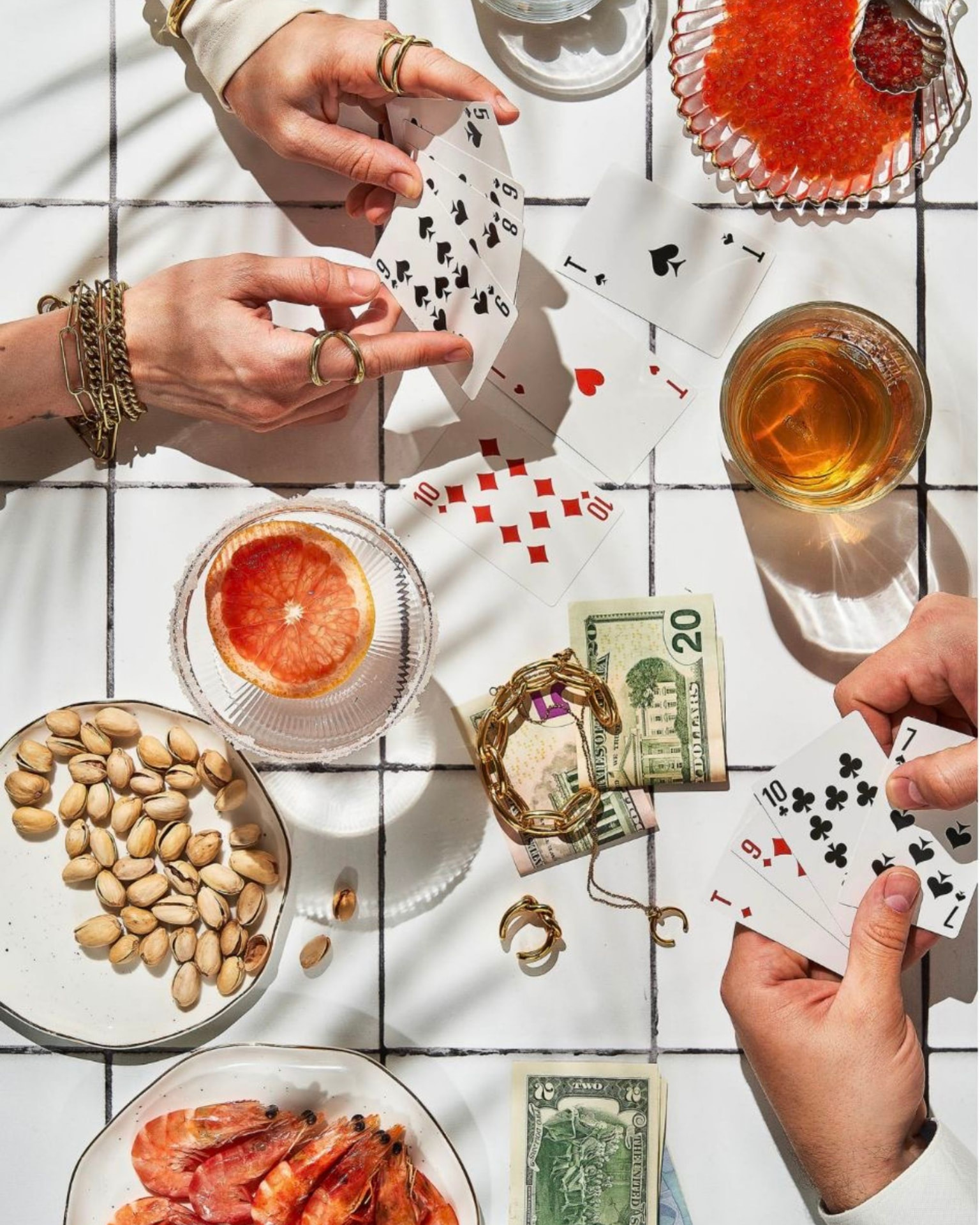 Zwei Hände halten Spielkarten am Tisch, dazu Getränke und Snacks