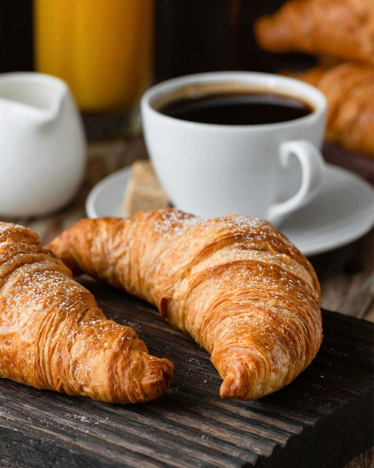 Croissants auf einem Holzbrett, dazu Kaffee und Orangensaft